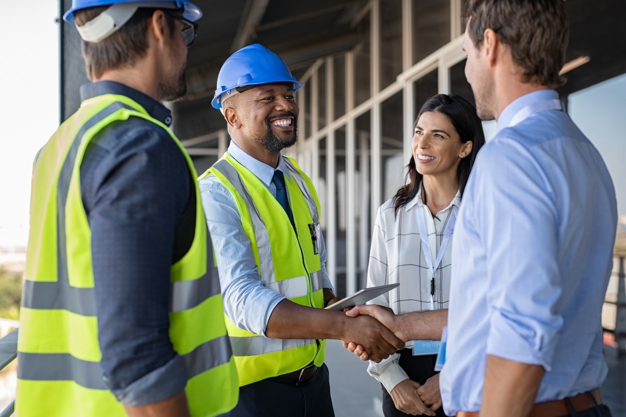 construction engineer in yellow vest shakes hand with man in blue shirt