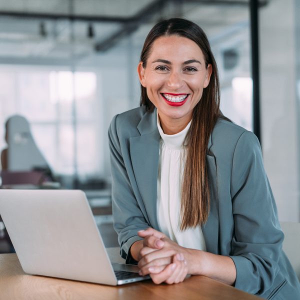 Successful businesswoman in modern office working on laptop. Portrait of elegant businesswoman sitting in her office looking at camera while using laptop.