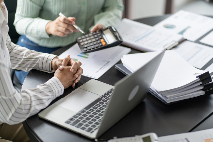 Two people reviewing financial documents with a laptop and calculator at a desk.