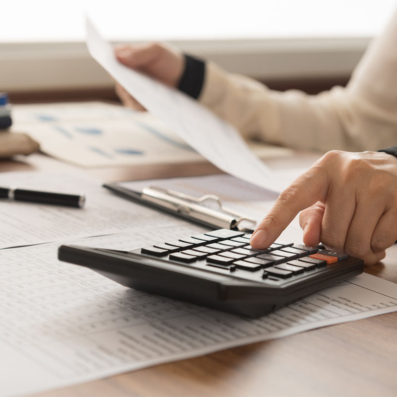 Person using a calculator at a desk with paperwork and a pen nearby.